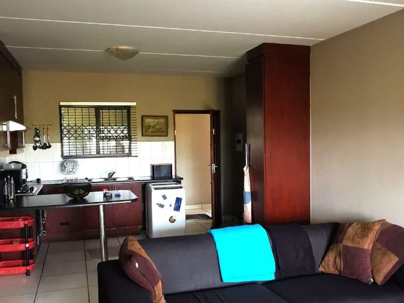 Open-plan living area featuring tiled flooring and a functional kitchen with built-in cabinetry and a security gate on the window.