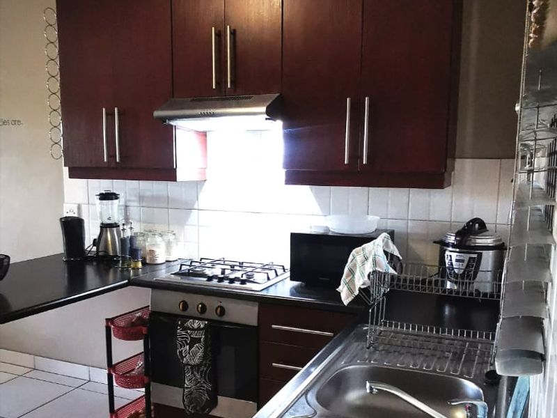 A functional kitchen featuring dark wood cabinetry, a stainless steel double sink, gas hob, built-in oven, and tiled backsplash.
