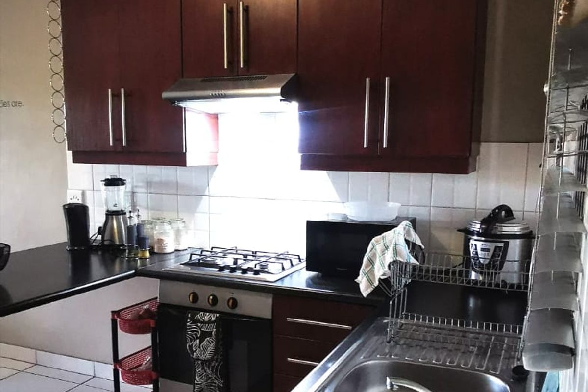A functional kitchen featuring dark wood cabinetry, a stainless steel double sink, gas hob, built-in oven, and tiled backsplash.