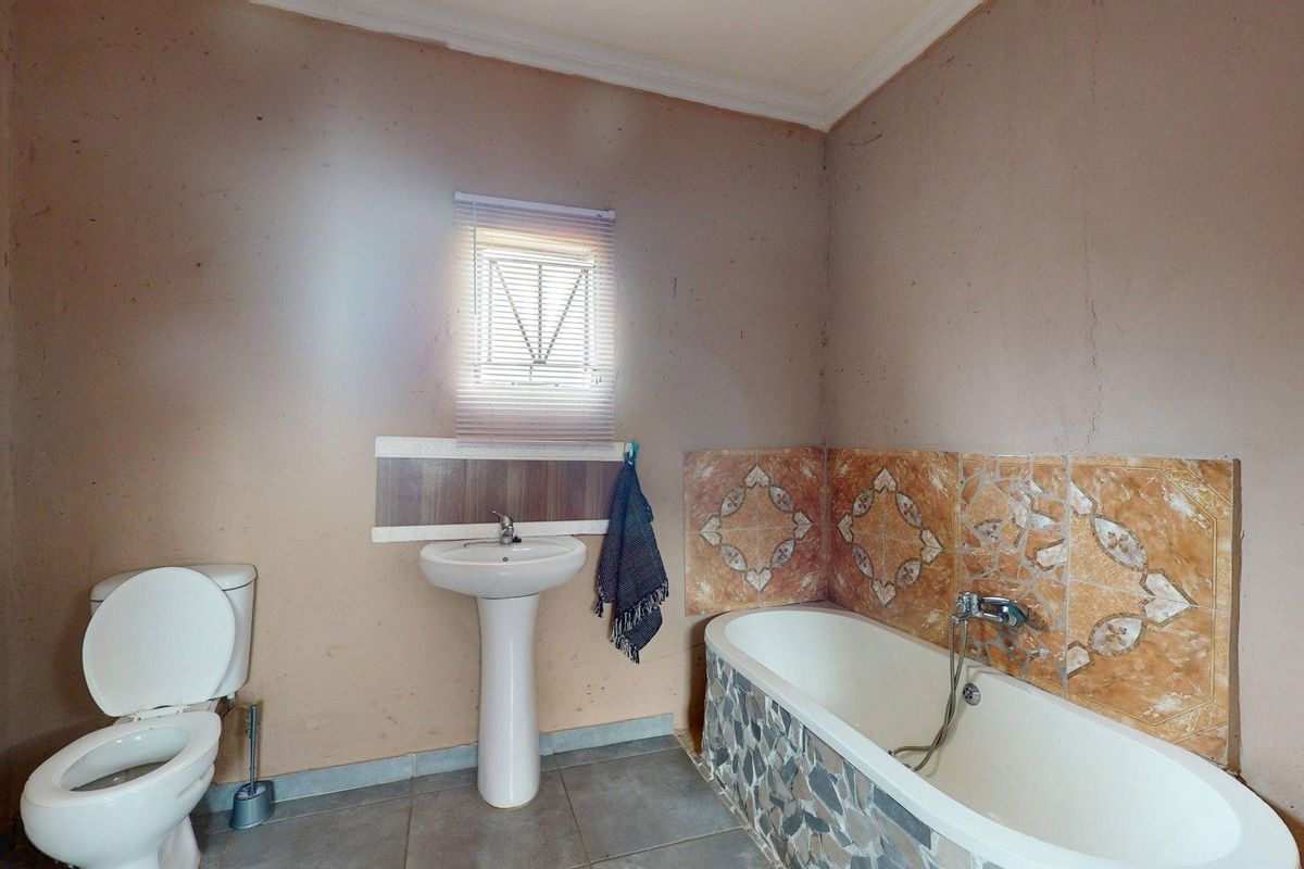 A dated bathroom featuring a pedestal basin, toilet, and bathtub with decorative tiled splashbacks and floor tiles.