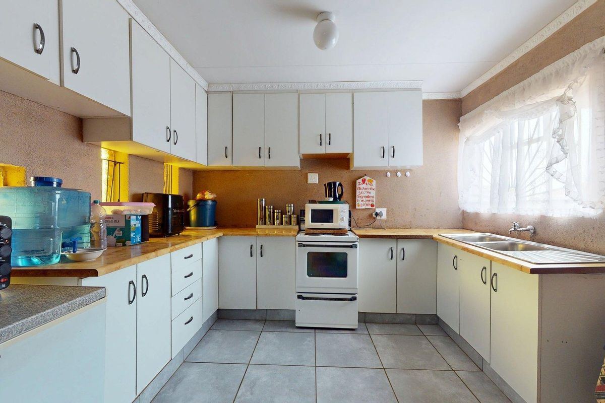 A functional kitchen featuring white built-in cabinetry, laminate countertops, a freestanding stove, and a double bowl sink with tiled flooring.