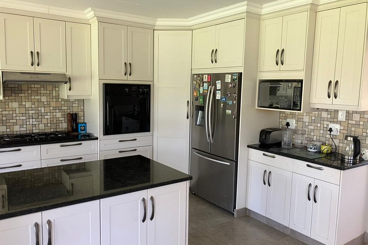 A well-maintained kitchen featuring white cabinetry, granite countertops, a central island, and built-in appliances including an oven, microwave, and gas hob.