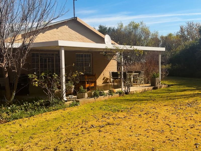 A rear view of the farm property featuring a covered patio area, brick exterior walls, and a spacious garden lawn.