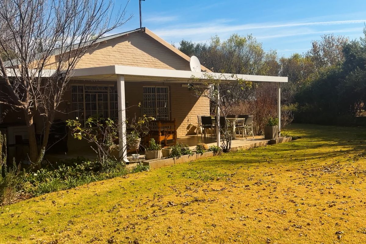 A rear view of the farm property featuring a covered patio area, brick exterior walls, and a spacious garden lawn.