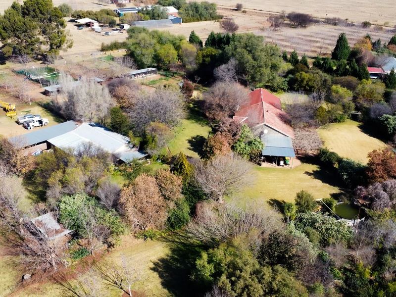 Aerial view of a farm property featuring multiple buildings, mature trees, landscaped gardens, and a swimming pool set within a rural landscape.