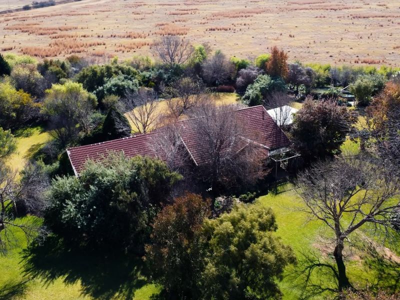 Aerial view of a farm property featuring a residence with a tiled roof set within a mature, landscaped garden and expansive surrounding fields.