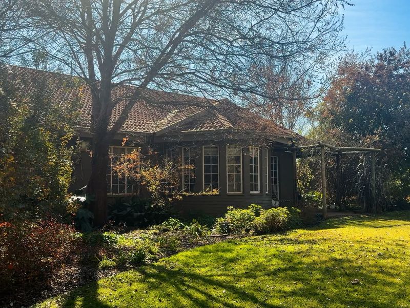 A view of the rear elevation of the farmhouse, featuring a tiled roof, bay windows, and a timber pergola overlooking a mature garden.