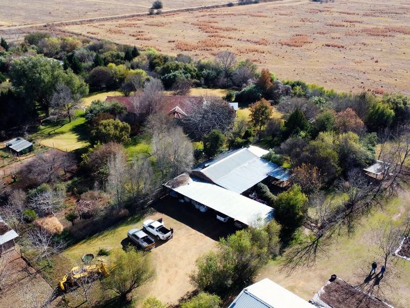 Aerial view of a farm property featuring multiple outbuildings, a large carport, and extensive surrounding land.