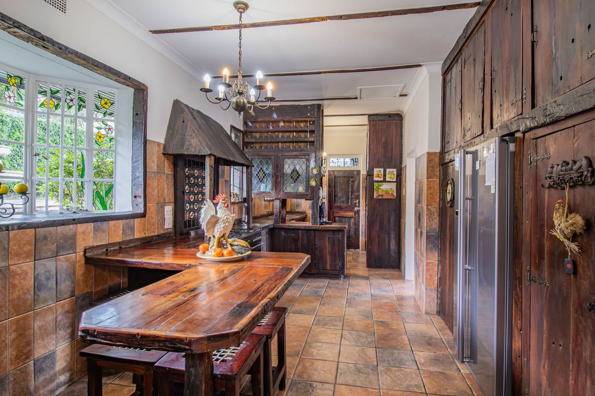 A rustic-style kitchen featuring extensive timber cabinetry, tiled flooring, a built-in breakfast bar, and unique stained glass windows with exposed ceiling beams.