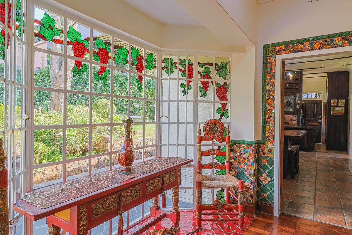 A sunlit living area featuring unique stained glass windows with grape motifs, decorative mosaic tile accents, and terracotta-style flooring leading to an adjacent room.