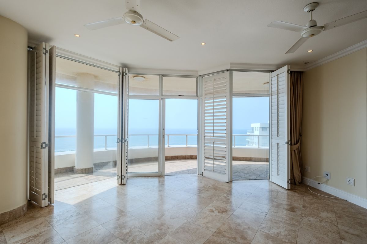 Spacious living area featuring large bi-fold doors opening onto a balcony with ocean views, complemented by tiled floors and ceiling fans.