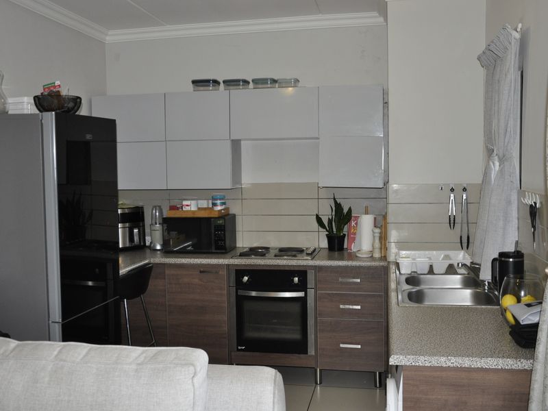 A functional kitchen featuring modern two-tone cabinetry, laminate countertops, a built-in oven with electric hob, and a double stainless steel sink.