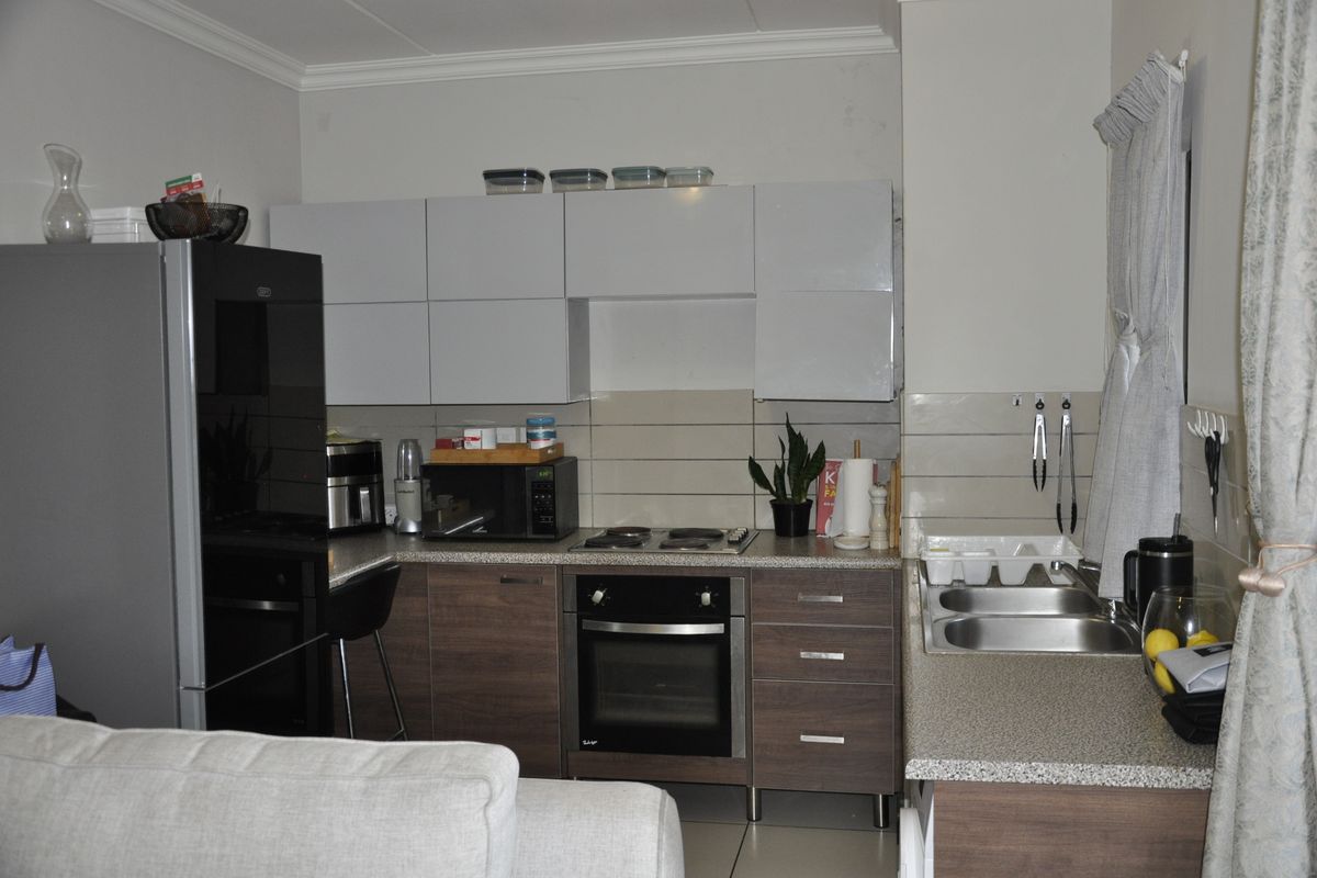 A functional kitchen featuring modern two-tone cabinetry, laminate countertops, a built-in oven with electric hob, and a double stainless steel sink.