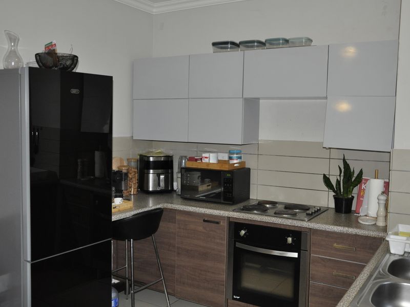 A functional kitchen featuring modern two-tone cabinetry, laminate countertops, a built-in oven with electric hob, and a double bowl sink.