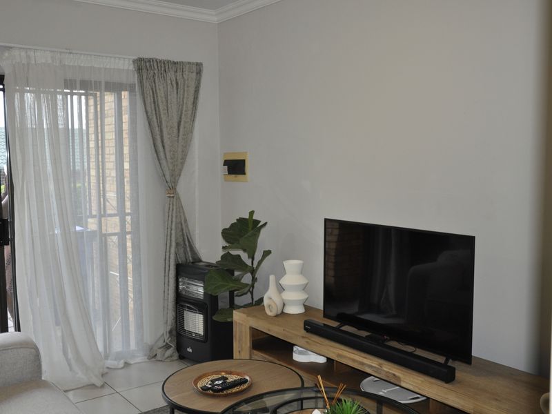 A bright living room featuring tiled flooring, coving, and a sliding glass door with an integrated security gate leading to the exterior.