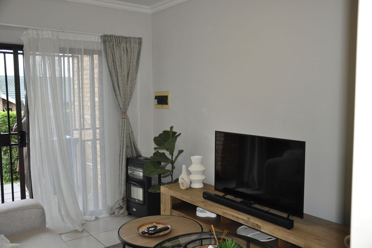 A bright living room featuring tiled flooring, coving, and a sliding glass door with an integrated security gate leading to the exterior.