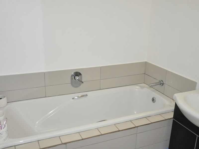 A functional bathroom featuring a built-in bathtub with wall-mounted mixer tap and tiled splashback, adjacent to a vanity basin.
