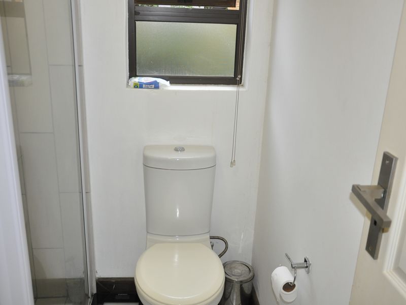 A functional bathroom featuring a standard toilet and a shower enclosure with a small window for natural light and ventilation.