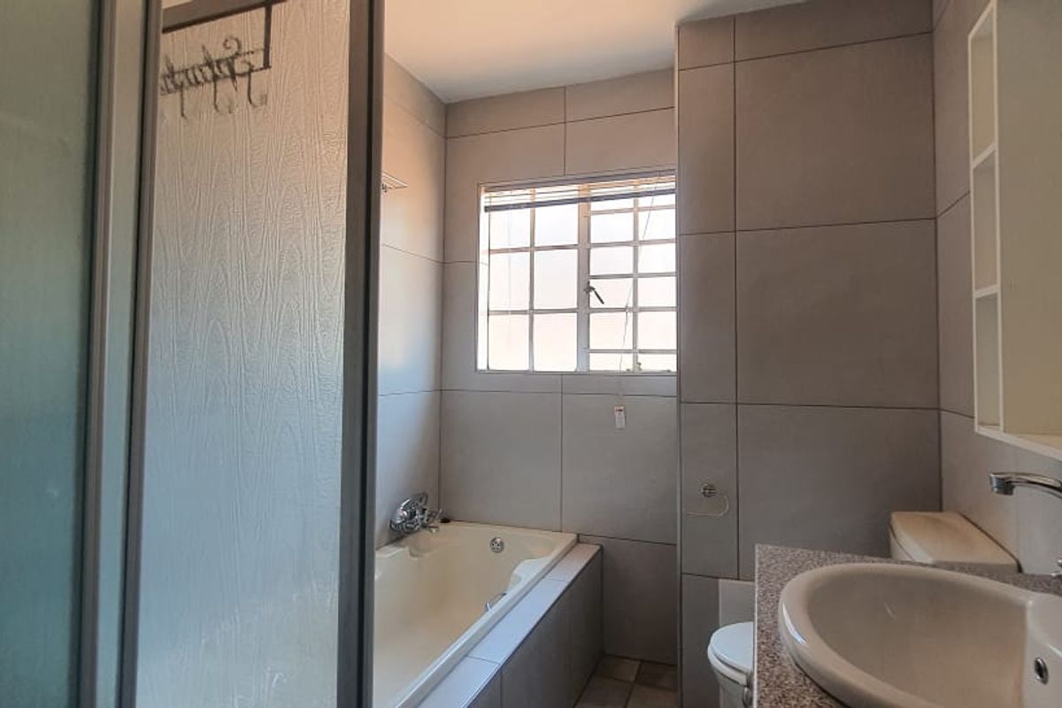 A functional bathroom featuring a built-in bathtub, separate shower enclosure, vanity basin with mixer tap, and neutral wall tiling.