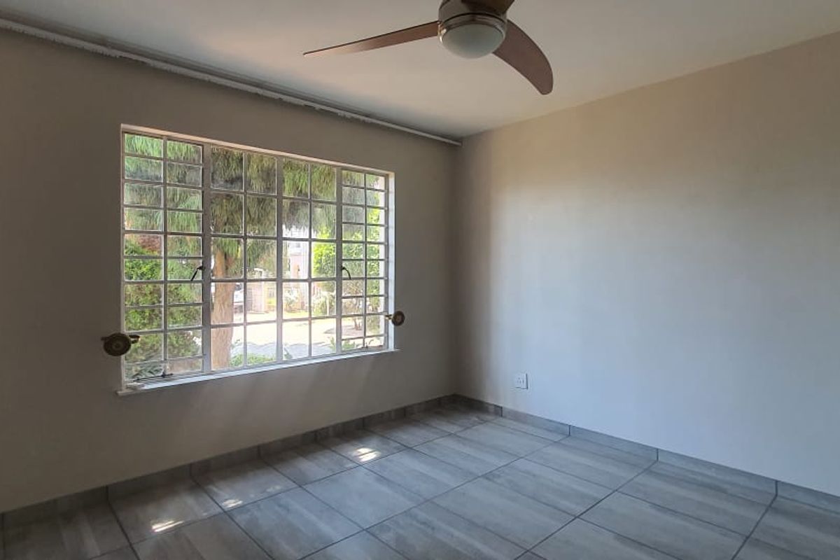 An empty bedroom featuring tiled flooring, a ceiling fan, and a large window providing natural light.