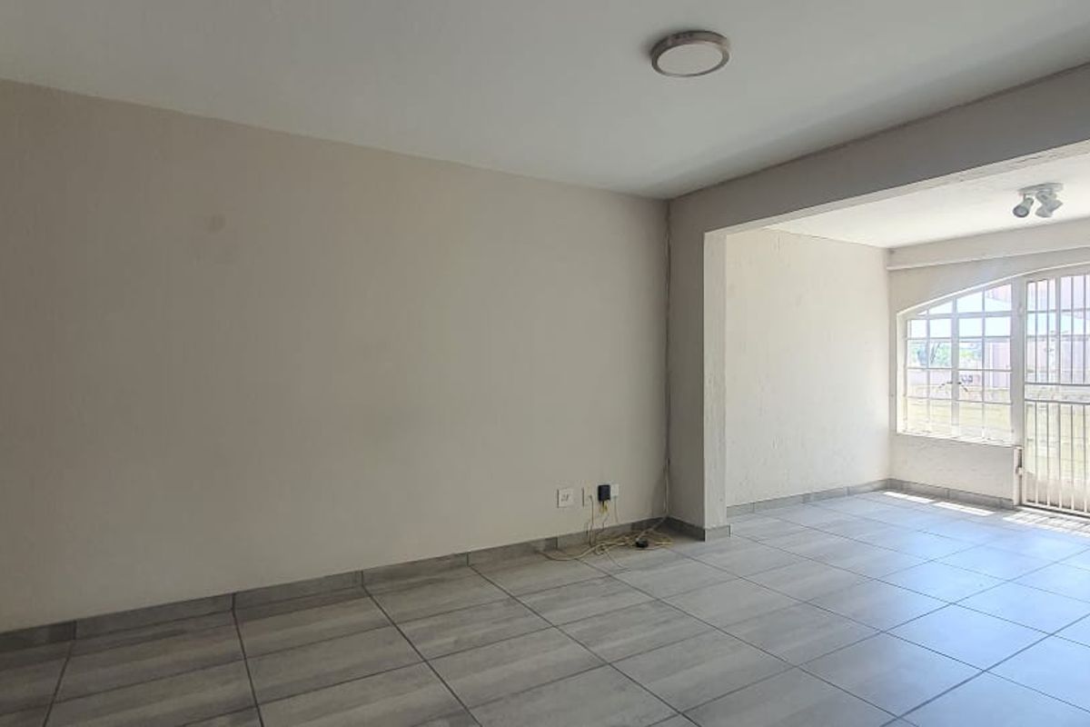 An empty, open-plan living area featuring neutral tiled flooring, a ceiling fan, and a large arched window with an integrated security gate.