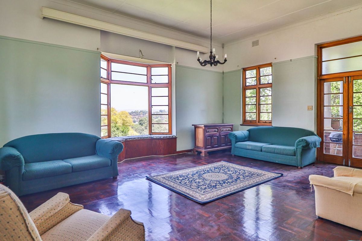 Spacious living room featuring original parquet flooring, large bay windows with scenic views, and direct access to an outdoor patio area.