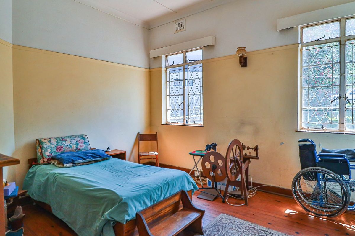 A bedroom featuring original timber flooring, large windows with security bars, and high ceilings, offering a classic layout ready for modernization.