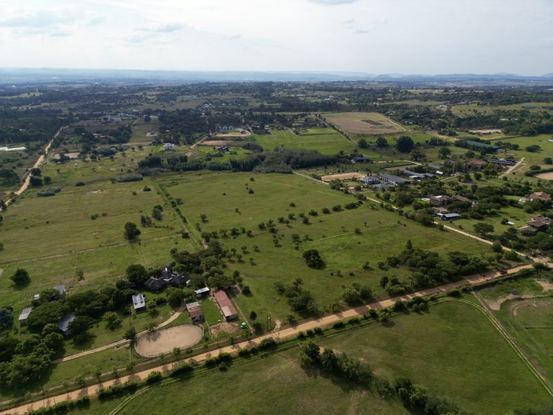 Aerial view of a large residential vacant land plot featuring open grazing areas, outbuildings, and an equestrian round pen in a rural setting.