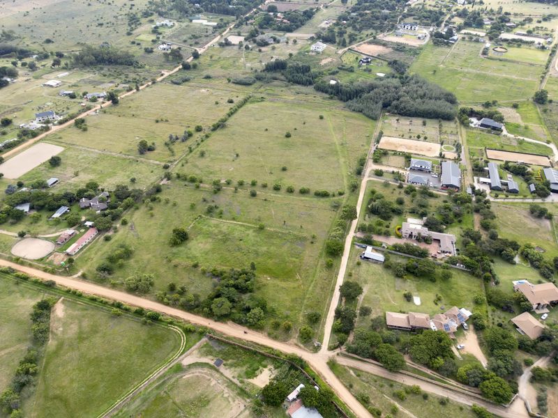 An aerial view of a large, undeveloped residential land plot situated within a rural estate setting with surrounding dirt roads and neighboring properties.