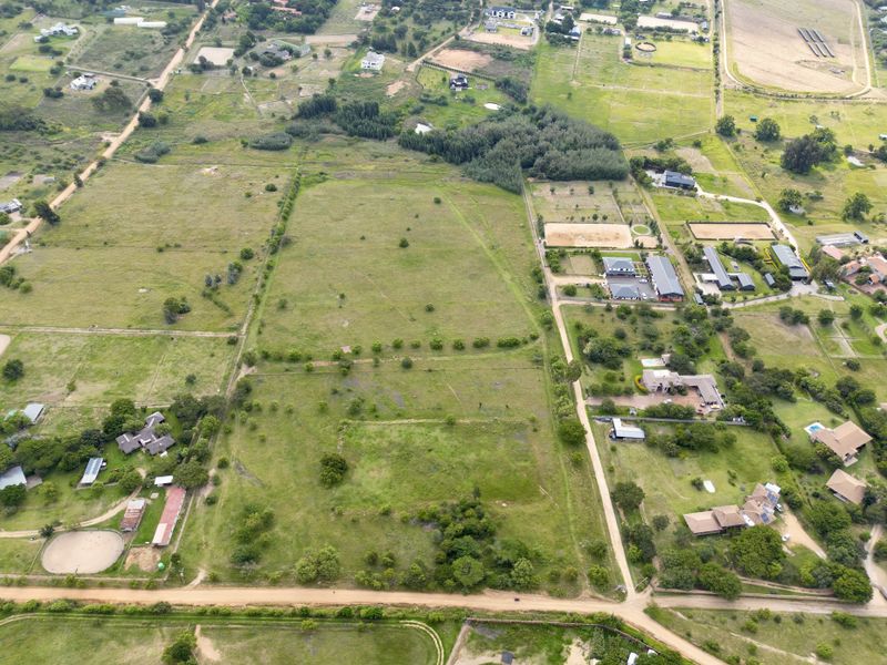 An aerial view of a large, vacant residential plot featuring open land, perimeter fencing, and access to a dirt road in a rural setting.
