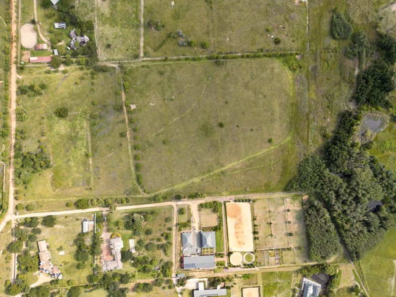 An aerial view of a large, vacant residential plot featuring open grassland, established perimeter fencing, and surrounding rural landscape.