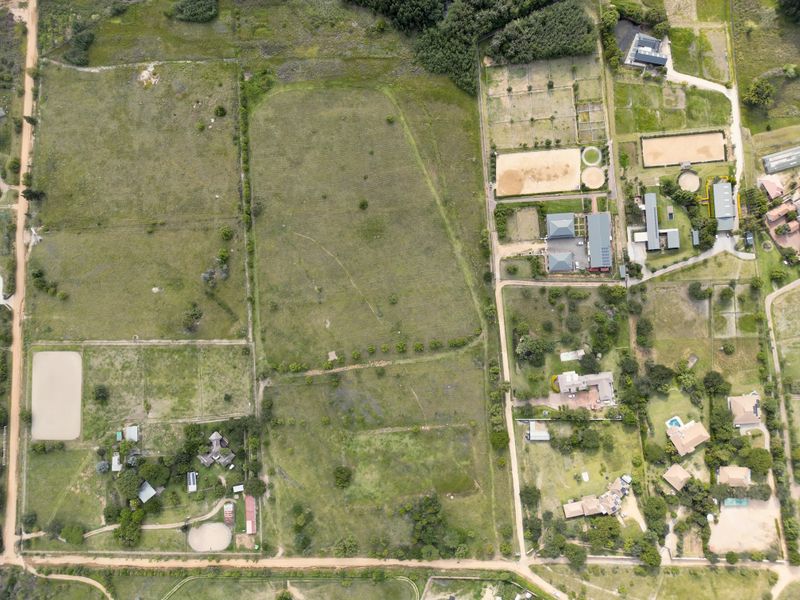 An aerial view of a large residential vacant land plot featuring open fields, established fencing, and surrounding rural infrastructure.