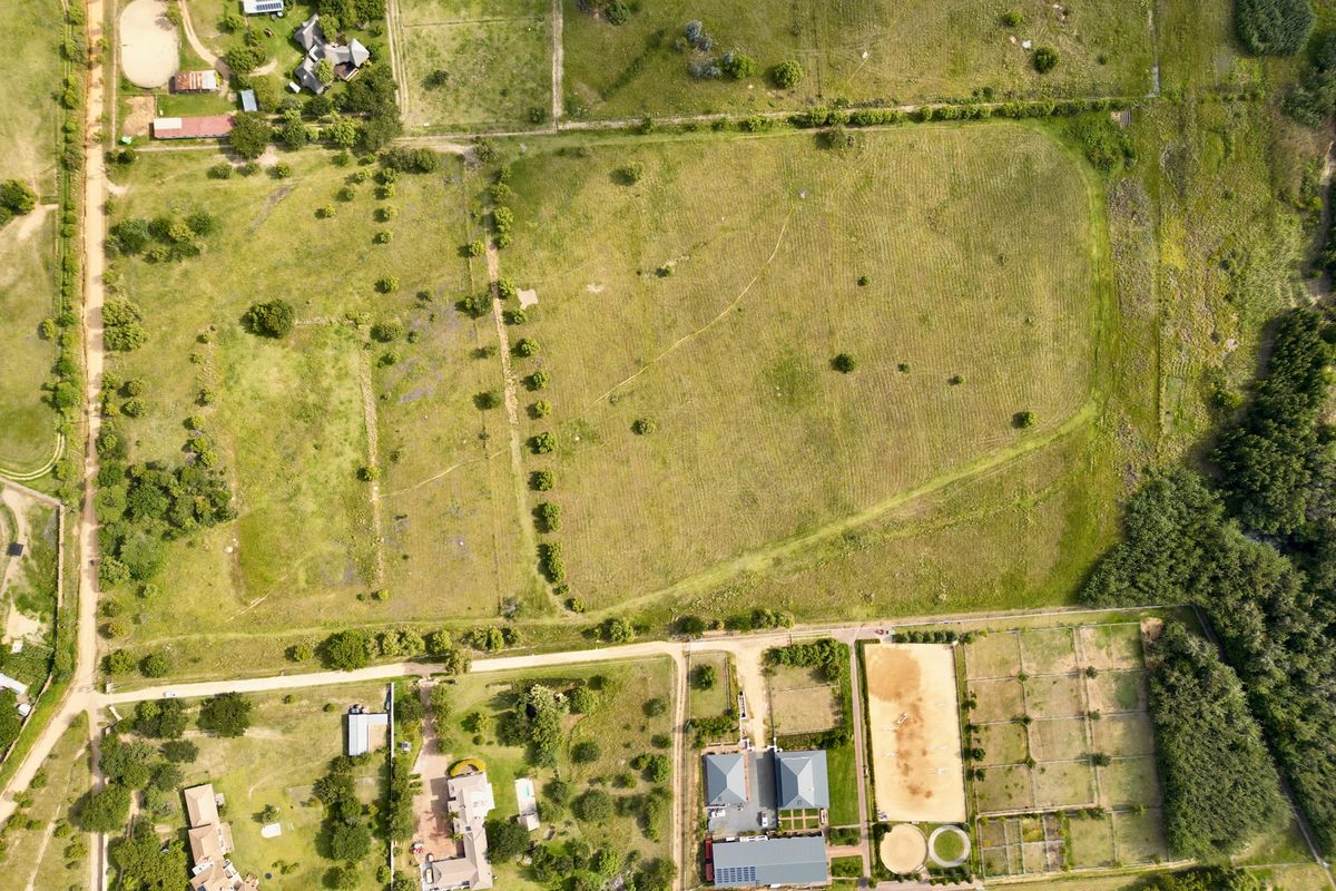 Aerial view of a large residential vacant land plot featuring open pasture, fenced paddocks, a riding arena, and established trees.