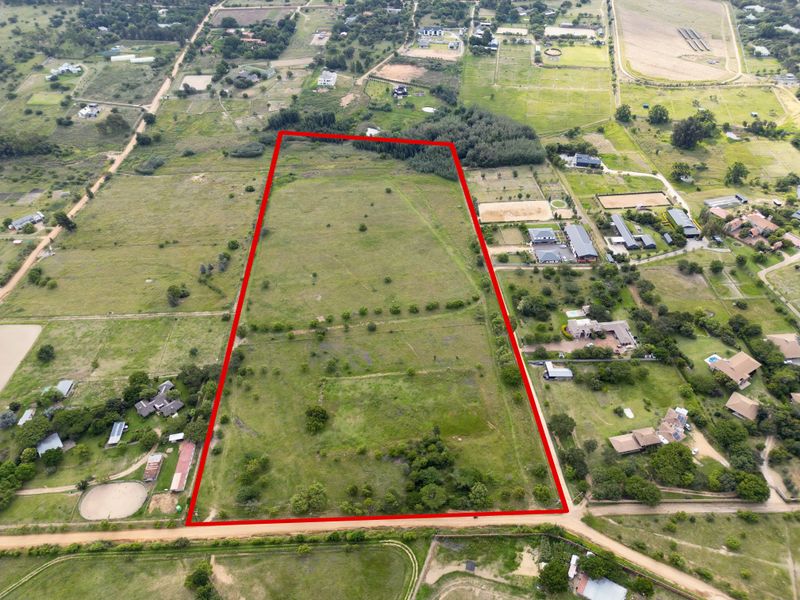 An aerial view of a large, rectangular vacant residential plot outlined in red, situated within a semi-rural estate setting.