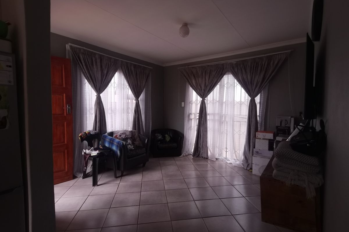 A living room area featuring tiled flooring and large windows with security gates, offering a functional space with natural light.