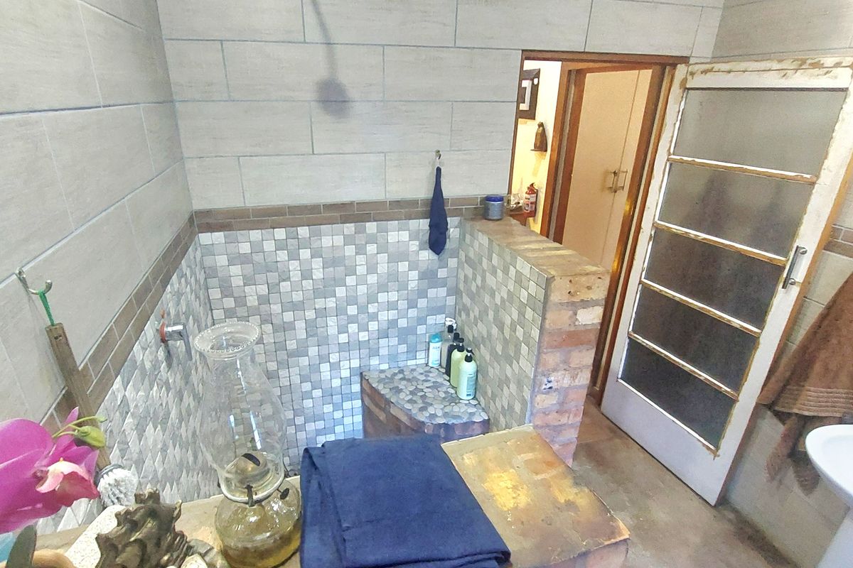 A bathroom featuring a walk-in shower with mosaic tiling, a brick-built vanity, and a pedestal basin, showing signs of wear and dated finishes.