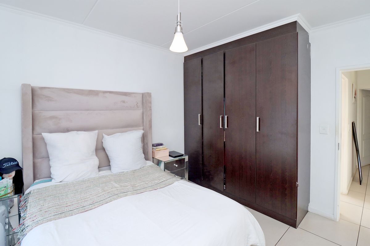 A well-maintained bedroom featuring dark wood built-in cupboards and neutral tiled flooring, offering a clean and functional living space.