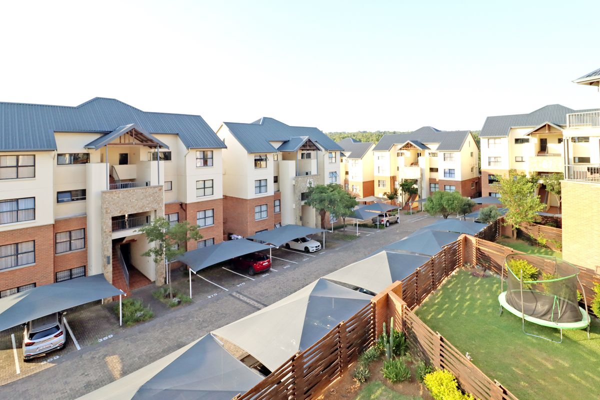 Aerial view of a modern apartment complex featuring paved parking areas with shade-cloth carports and landscaped garden spaces.
