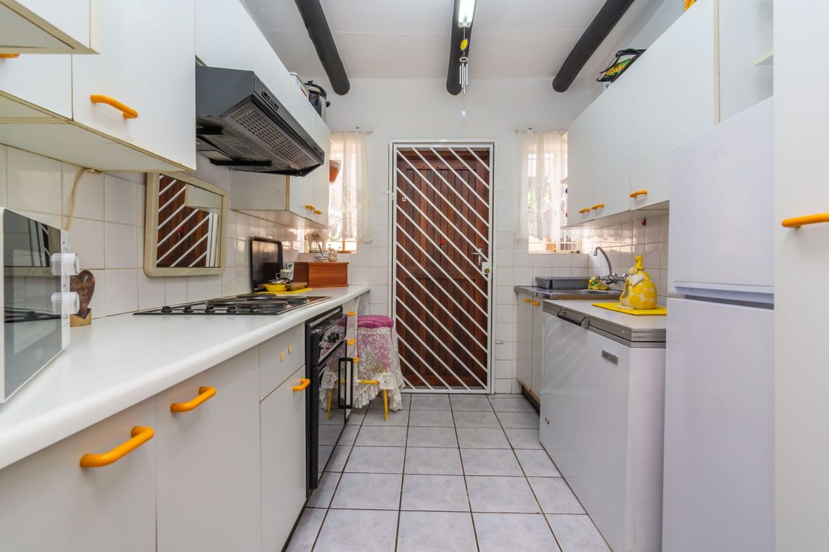 A functional galley-style kitchen featuring white cabinetry, a gas hob, built-in oven, and tiled flooring with direct access to an exterior door.