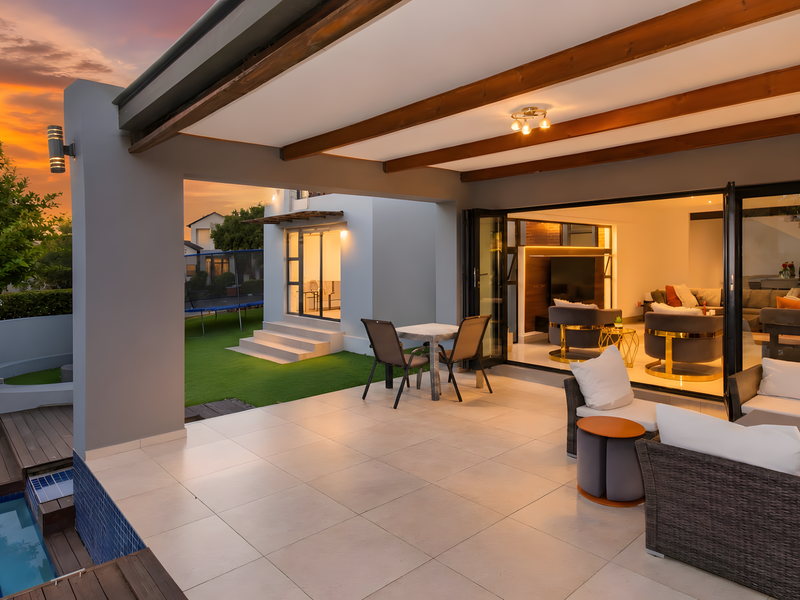 Spacious covered patio featuring tiled flooring, exposed timber beams, and seamless bi-fold doors leading to a modern living area and swimming pool.