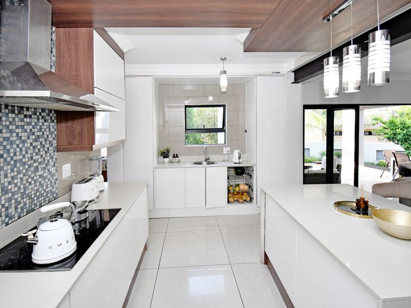 Modern kitchen featuring sleek white cabinetry, stone countertops, a central island, and high-end integrated appliances with a stylish mosaic tile backsplash.