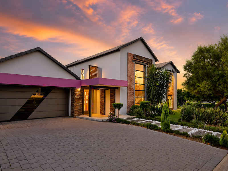 Modern double-story residence featuring a paved driveway, double garage, stone and brick accents, and a beautifully landscaped front garden at sunset.