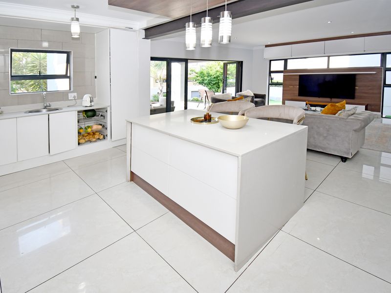 Modern open-plan living area featuring a sleek kitchen with a central island, quartz countertops, and seamless flow to the lounge and outdoor patio.