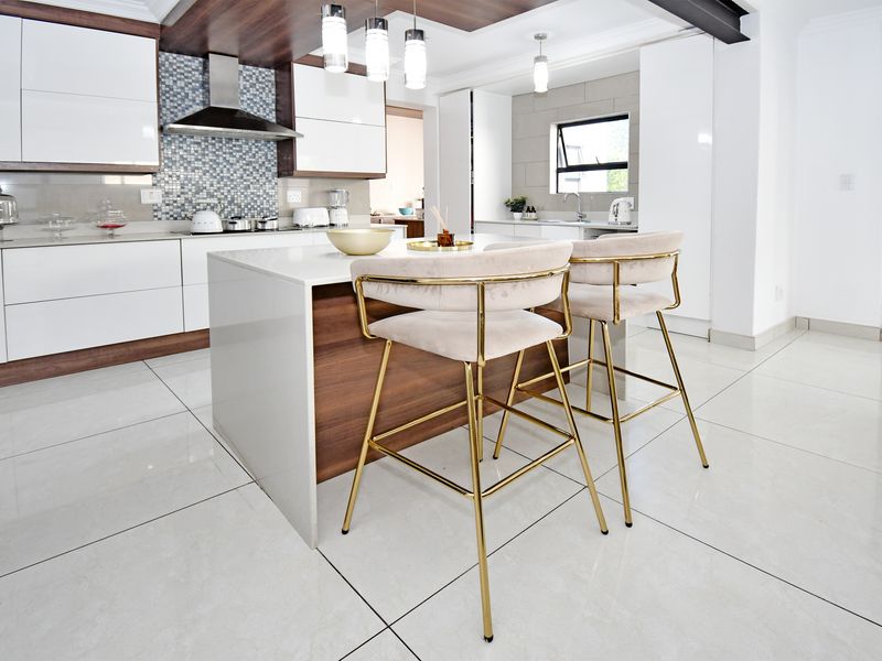 Modern kitchen featuring a central island with stone countertops, high-gloss cabinetry, mosaic backsplash, and sleek porcelain floor tiles.