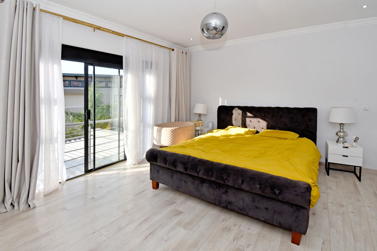 Spacious bedroom featuring light-toned laminate flooring, crown molding, and a large sliding glass door providing access to an outdoor balcony.