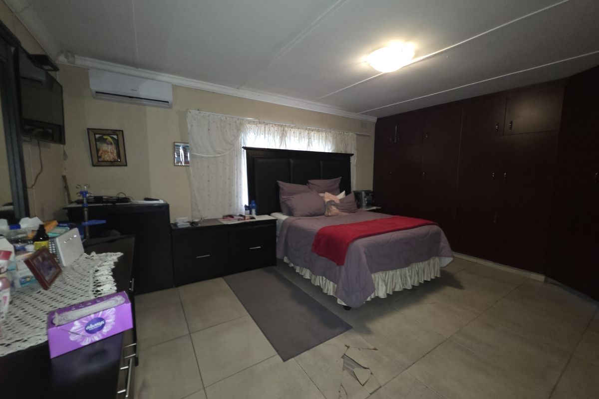 Spacious bedroom featuring built-in dark wood cupboards, tiled flooring, and a wall-mounted air conditioning unit.