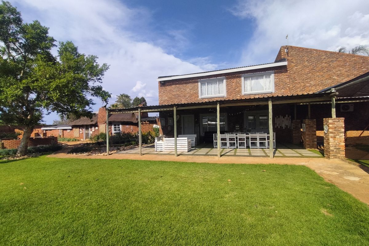 Rear view of a face-brick small holding property featuring a spacious covered patio area overlooking a well-maintained lawn and garden.