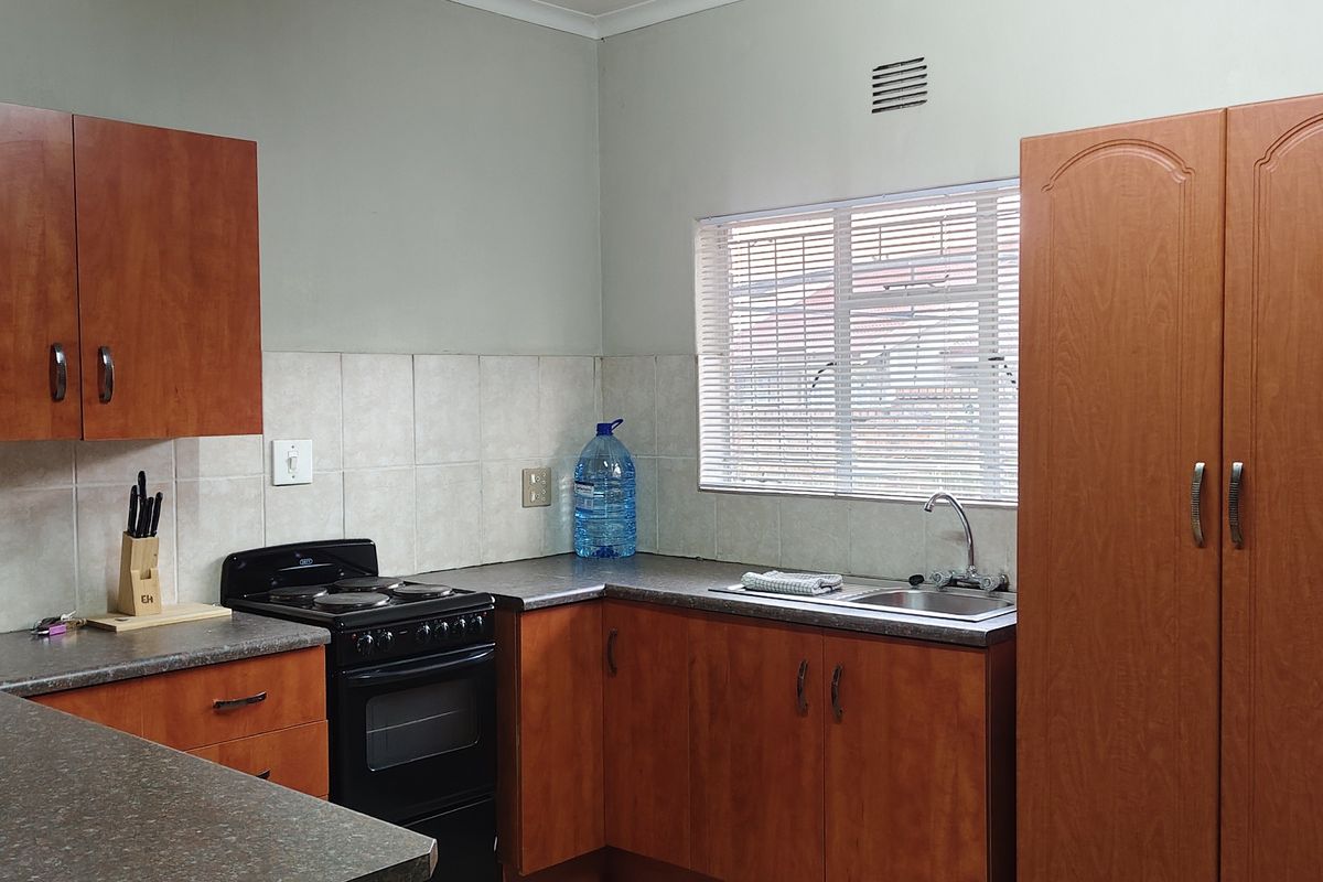 Functional kitchen featuring wood-look laminate cabinetry, dark countertops, a stainless steel sink, and a freestanding stove with a tiled backsplash.