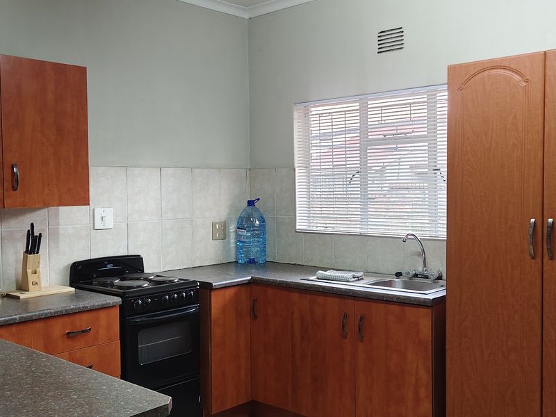Functional kitchen featuring wood-look laminate cabinetry, dark countertops, a stainless steel sink, and a freestanding stove with a tiled backsplash.