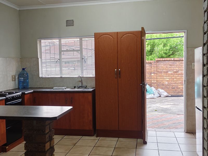 Functional kitchen featuring built-in wooden cabinetry, tiled flooring, a brick feature wall, and direct access to an outdoor paved area.